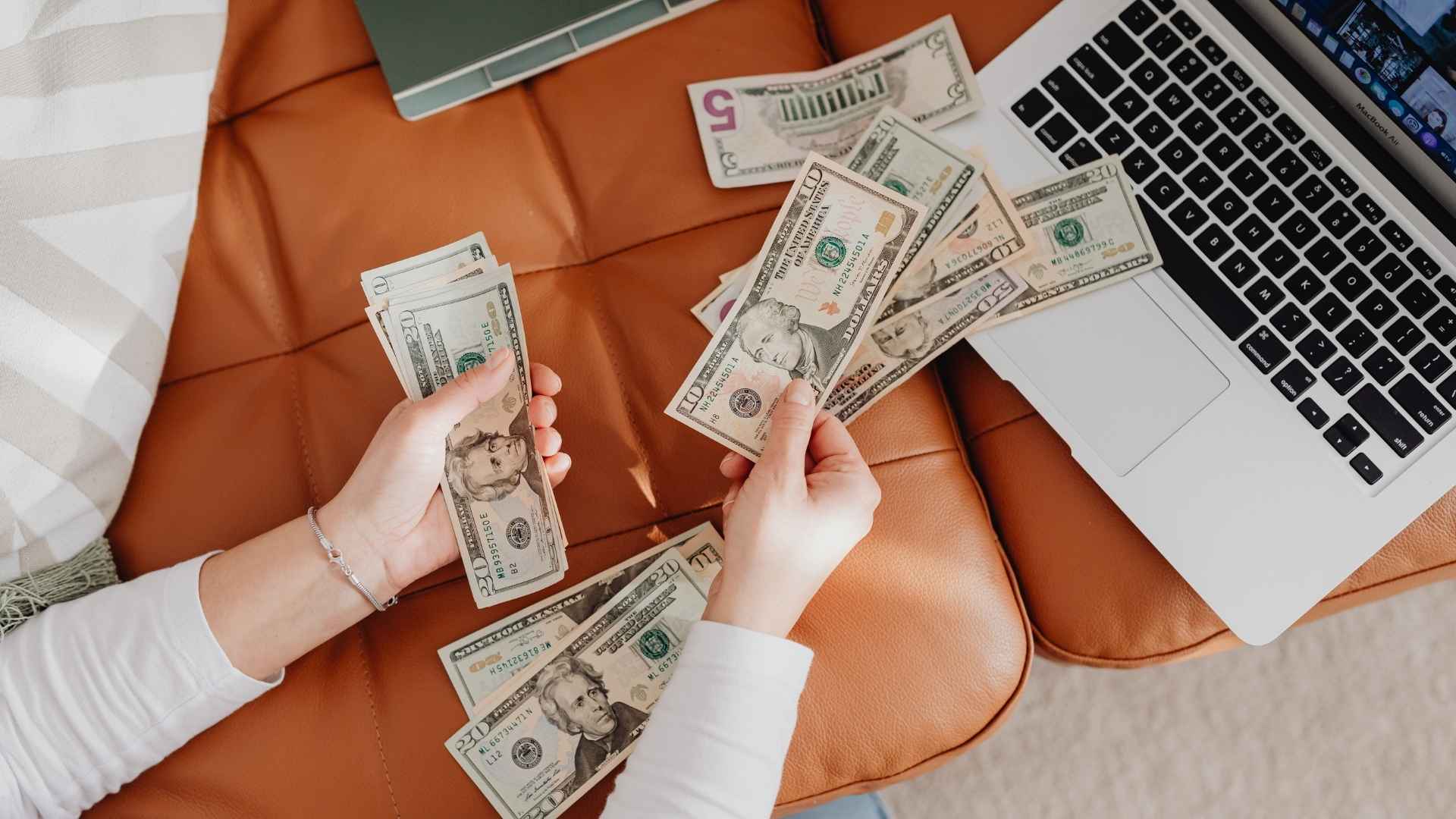 close-up woman counting dollar bills in front of her laptop