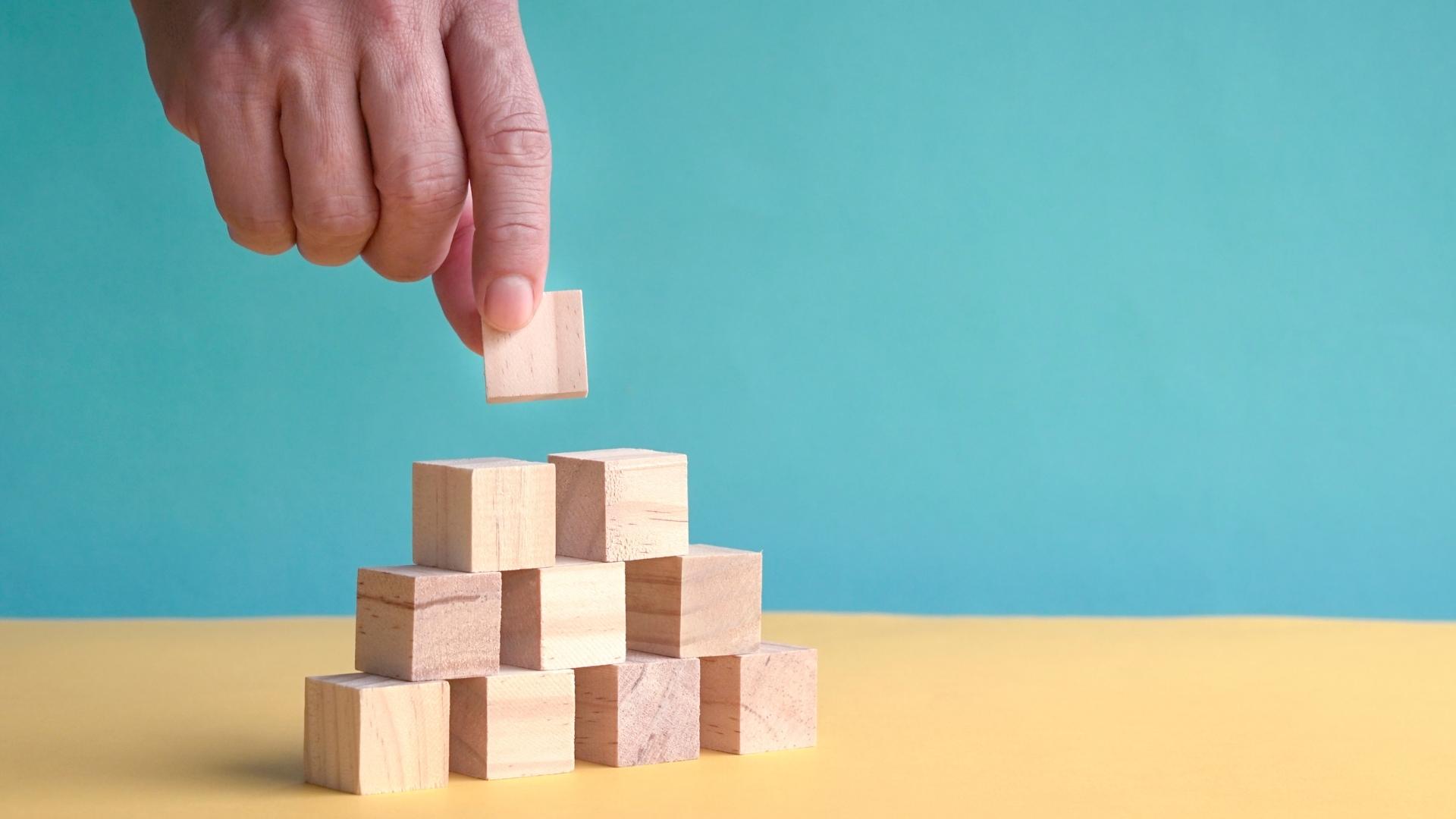 hand arranging a pyramid of stacked blocks