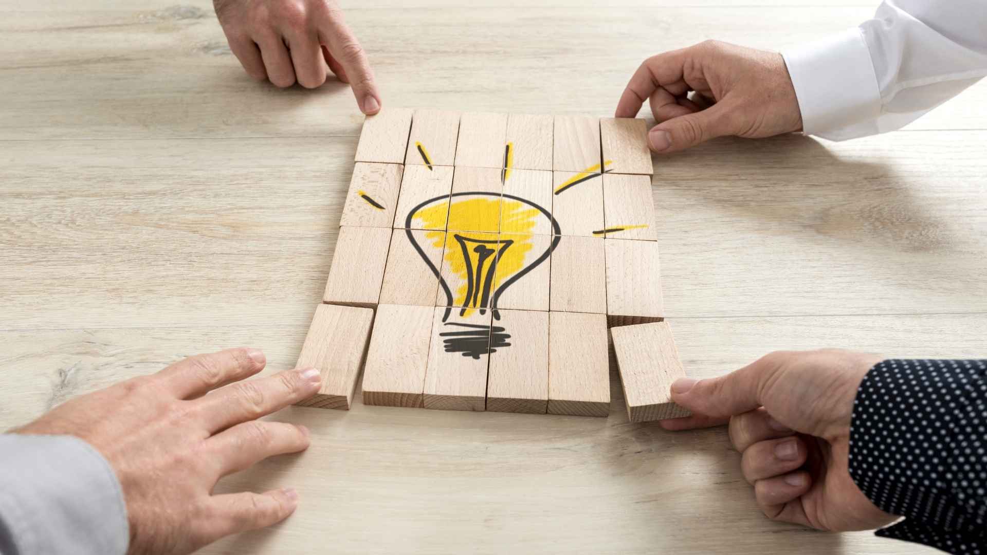 people holding pieces of wooden block forming a lightbulb