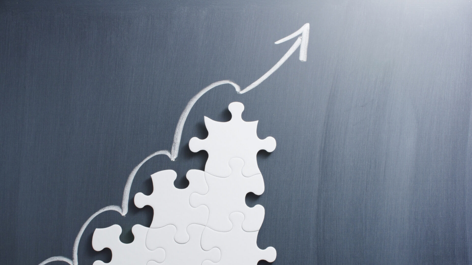 Steps shaped jigsaw puzzle and up arrow on blackboard.