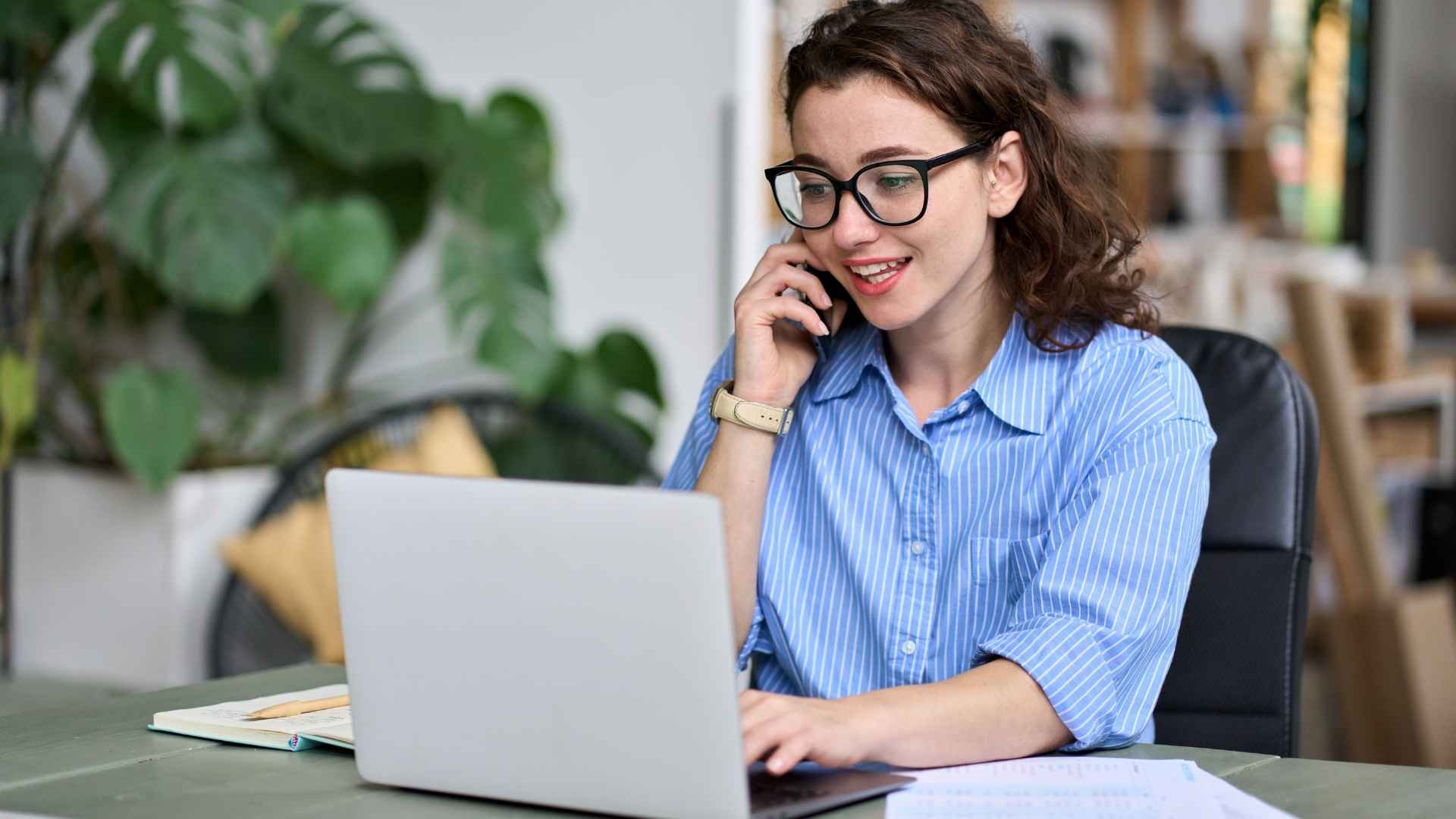 woman calling on her phone while looking at the laptop