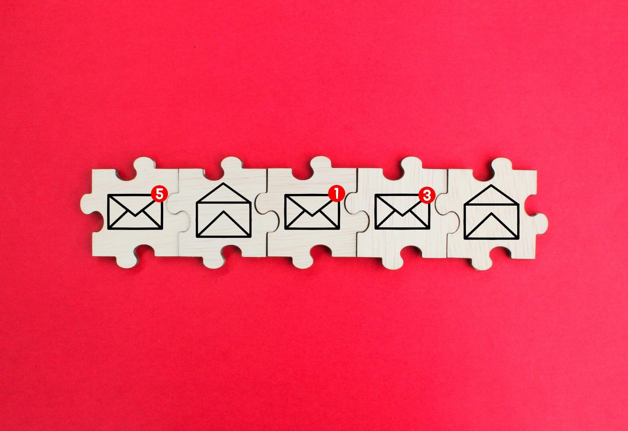 A series of wooden puzzle pieces on a red background, each piece with icons depicting read and unread email envelopes, symbolizing email management.