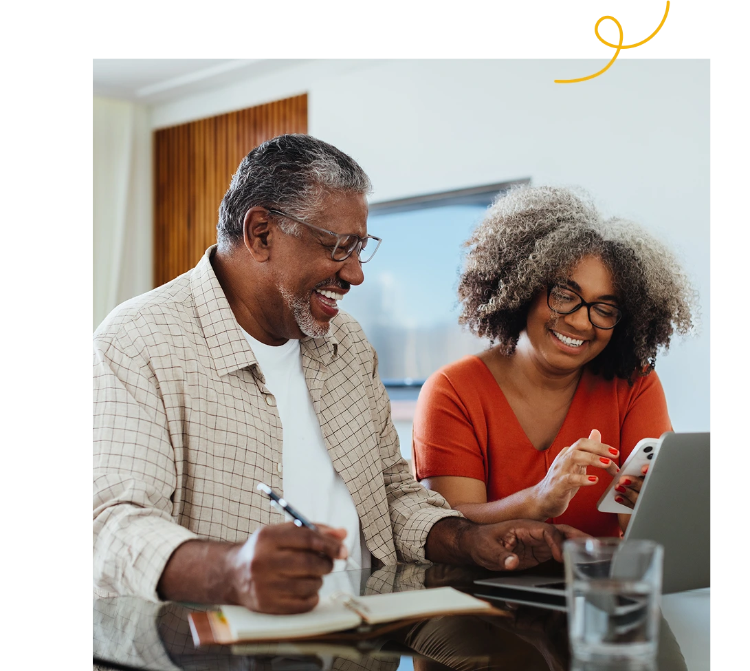 A joyful older couple working or learning together using a laptop and a smartphone