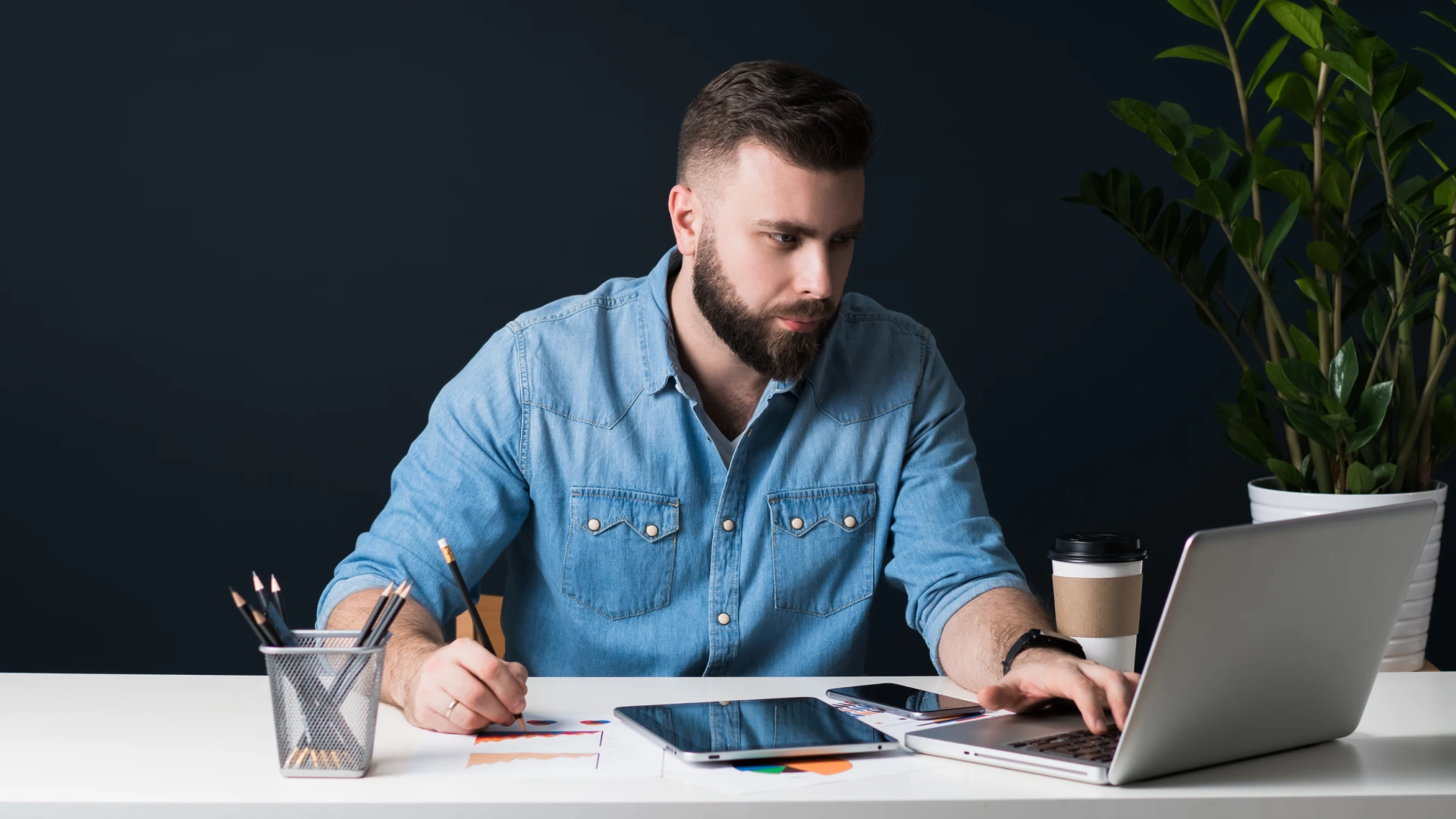 Front view. Young bearded businessman is sitting in the office at desk